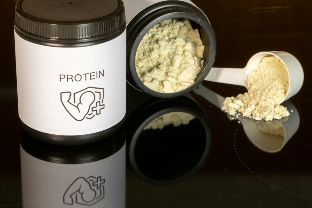 A scoop of whey protein powder next to a jar on a kitchen counter
