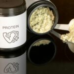 A scoop of whey protein powder next to a jar on a kitchen counter